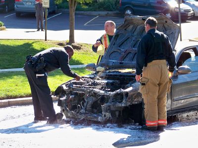 Various fire and police officials inspect the car following the fire department's completing its work. As you can see, the front of the car pretty much melted away.