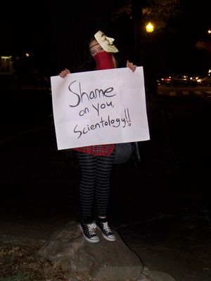 This Anon held a sign saying, "Shame on you, Scientology!" while wearing a bandanna over her face and the Guy Fawkes mask to the side.