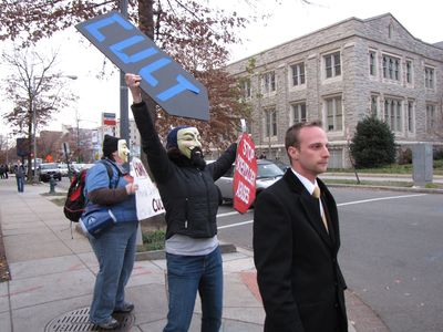 Note the "CULT" sign pointing right at the man, and the "End Scientology Abuses" sign in her other hand.