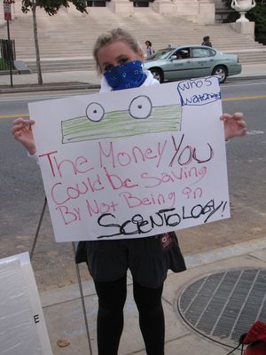 Little JB holds up a sign with the Geico money being talking about all the money they'll save if they leave Scientology.