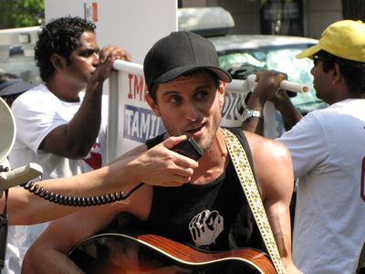 A man plays a guitar, and sings through a bullhorn.