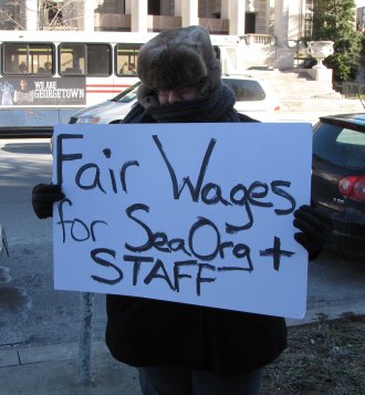 HT raids maskless, with a "Fair wages for Sea Org" sign.