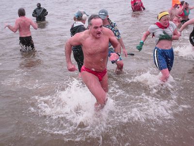 A man comes out of the water wearing a speedo. Honestly, this is probably the best way for the menfolk to plunge. A little something to cover the necessary areas, and thus no big, baggy suit to cling to your body and be cold against your skin. That way, the warm, dry towel afterwards feels that much warmer since there's no big pair of wet shorts to get in the way.