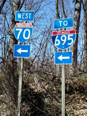 Interstate shields posted at the eastern end of the park and ride, adjacent to the westbound roadway. Note the lack of a "TO" sign over the I-70 shield. That is the indication that the road is actually I-70 all the way into and through the park and ride and that the earlier sign is incorrect, because signage indicates that westbound I-70 starts in the park and ride. If the earlier sign was correct, and the I-70 designation actually ended at I-695, there would be a "TO" sign over the I-70 shield, similar to the "TO" sign over the I-695 shield.