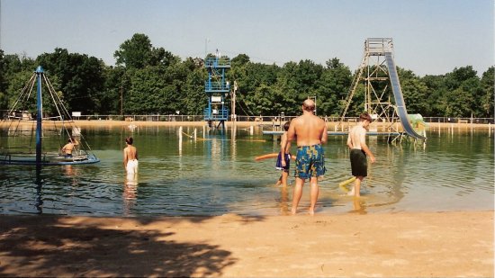  This is the view from the east side of the lake, across the lake from the beach house (i.e. this was the "far side" of the lake).  This photo is from 1997 or later, based on the absence of the original beach house.  This photo shows most of the amenities in the lake, including a merry go round (far left), the tower with zip lines (center, in the distance), the big slide (right side of photo), and Clyde the Slyde (behind the big slide).