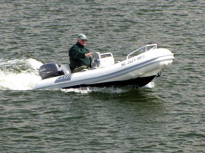 A man drives a powerboat down the harbor, seen from near the Compromise Street bridge.