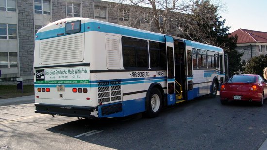 Harrisonburg Transit bus making a passenger stop on the JMU campus next to an illegally-parked car.