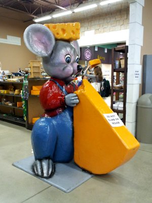 A giant mouse eating a big piece of cheese, while wearing a cheese hat.