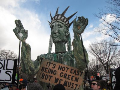 The Statue of Liberty, with a sign saying, "It's not easy being green (but we must)."