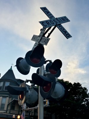 Railroad crossing signal with two sets of lights and crossbucks. The lights and crossbuck facing left are for traffic on Main Street, while the other set, facing approximately forward, is for traffic on Liberty Street.