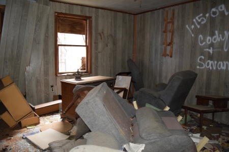 The family room, with wood paneling, a bunch of couches, and a broken-out television.