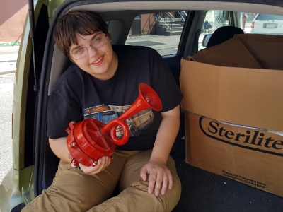 Elyse sits on the tailgate in Philadelphia, holding up a vintage fire alarm horn, October 2016.