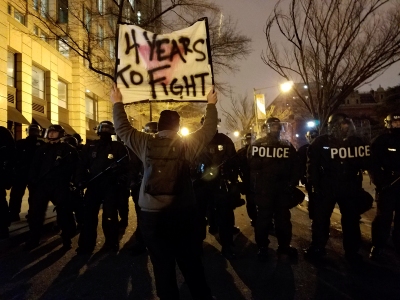 Holding a "4 Years To Fight" sign in front of a row of police in riot gear.