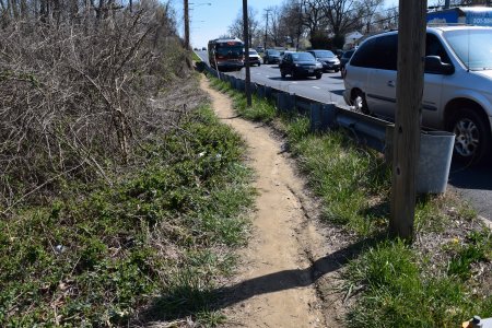 Well-worn desire path along the side of westbound Veirs Mill Road.  There are no sidewalks in this area, and this path runs from Havard Street all the way to the subject crossing at the bottom of the hill.