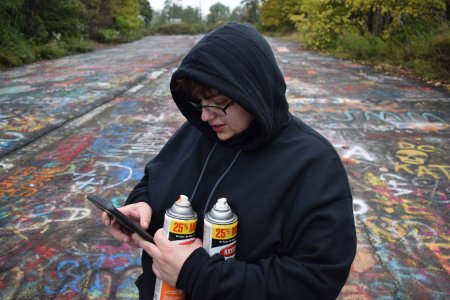 Elyse holds her spray paint cans while checking her phone.