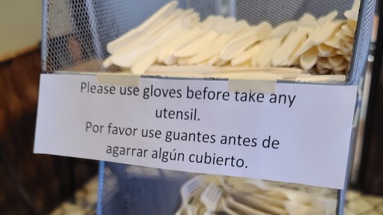 Sign at a restaurant, requesting that people put on the provided gloves before taking a utensil.