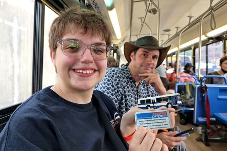 Elyse holds up Fred's model DASH Orion V, along with a card describing what it is.  Both of these were destined for a display at DASH headquarters.