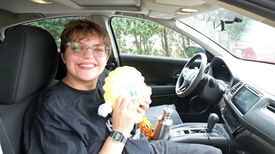 Elyse, in the car and holding a Scrub Daddy plush. Woomy is sitting in the console, stewing about something.
