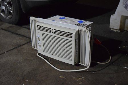 A window air conditioning unit on the sidewalk.  A note taped to it read, "CFC recovery for Department of Sanitation".