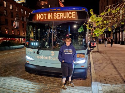 Elyse poses for a photo with a New Flyer Xcelsior bus, while the operator unintentionally photobombs us.