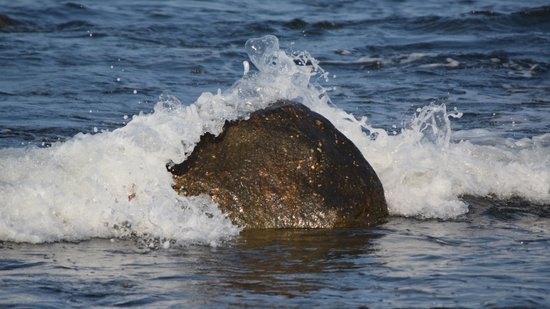 A wave splashes over a boulder in the water at Montauk Point.