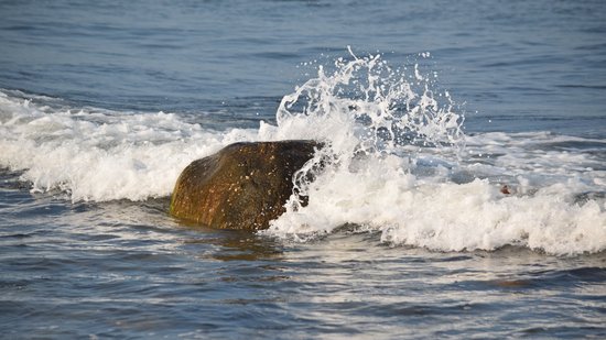 A wave splashes over a boulder in the water at Montauk Point.