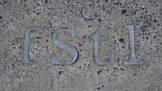 Metal "fstl" letters embedded in the concrete of the sidewalk in front of Four Seasons Total Landscaping's main entrance.