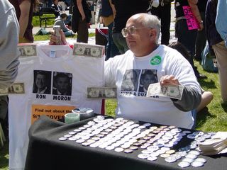 A gentleman sells buttons and t-shirts, and gives out fake dollar bills with various sites' URLs on them.