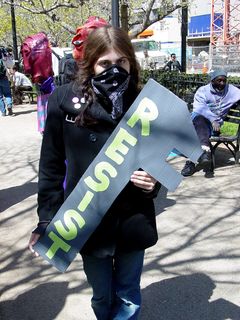 A masked woman holds up a cardboard monkey wrench, one of a number of props made in advance by the organizers. The theme of this demonstration was "A Better World Is Under Construction", and as a result, the props took the shape of various tools and construction equipment. Creative!