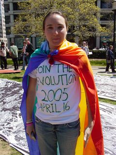 This woman wears a rainbow-colored "Peace" flag, while wearing a hand-painted shirt that says, "Join the Revolution 2005 April 16".