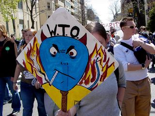 This sign portrays the World Trade Organization (WTO) as a devil, smoking a cigarette labeled "human rights".