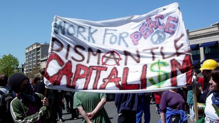 The sign seen from behind in the previous movie reads, "Work for peace, dismantle capitalism".