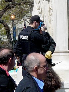 The police officer films demonstrators from the center of Dupont Circle. I remember that on J20, the black bloc had the center of the park, since we got there first. The police set up around the perimeter. This time, since Dupont Circle was part of a predetermined permitted march, the police got dibs on the center. Still, with the officer filming using his Canon camcorder, that just irritated me...