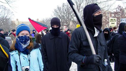 A black bloc, as mentioned earlier, had gathered around the back of the group, but closer to the stage than the police cars. This black bloc was definitely more hardcore than I was accustomed to, as a number of them had items for defending against pepper spray and tear gas close by.