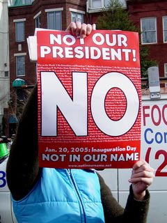 Someone holds up a poster reading, "Not our President!" and "Not in our name". The poster also shows the URL for the Not In Our Name Project.