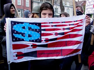 This person holds up a flag showing a twist on the United States flag showing what is perceived as the real truth behind the war on terror. The flag also advertises truth-now.com.