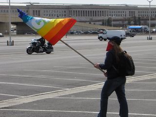 A masked woman waves a peace flag through the Pentagon parking lot.