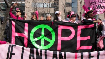 Code Pink demonstrators hold up multiple banners.