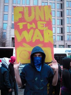 A masked individual holds a hand-painted "Funk the War" sign.