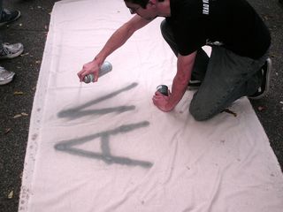 Spray painting a message on a banner. This banner would ultimately read, "ANTI-CAPITALISTA".