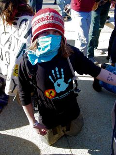 This masked person shows off two things: the Genocide Intervention Network shirt that they are wearing, and also the number for legal assistance for J27 that was written on their arm. Writing numbers for legal help on one's arm is standard practice for many activists. This way, because if it's written directly on the skin, it's not likely to get lost in the chaos of an arrest.