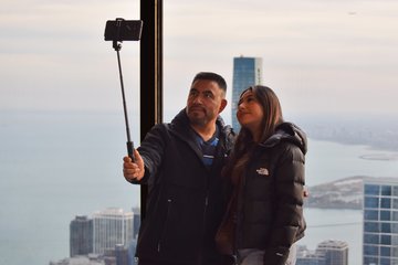 A couple uses a selfie stick in front of one of the windows.