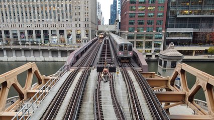 Two Brown Line trains cross the bridge over the river.