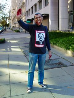 A person waves while wearing a George W. Bush mask, and t-shirt featuring an image of George W. Bush and the words "International Terrorist". The Bush mask had some of the teeth modified to look like fangs, and had fake blood below the mouth. Additionally, the person's hands were covered with fake blood. Reminds me of the "Bloody Hands" sign shown at the anti-war procession on October 2.