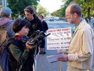 Aside from the main activity at the hotel, some took part in other activities. One woman takes a moment to interview a man carrying a sign comparing George W. Bush, John Kerry, and Ralph Nader on bringing the troops home, health care for all, and a living wage.