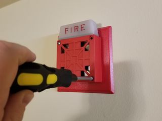 Unscrewing the fire alarm from the wall, leaving only the anchors in place.