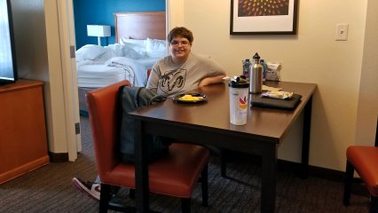 Elyse sits at the table in our room at the Residence Inn with her breakfast, which was a full-on hot breakfast where you served yourself, which I was kind enough to bring up for her.