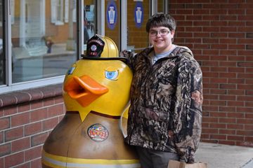 Here, Elyse poses for a photo with a duck sculpture, where the duck is dressed as a firefighter.