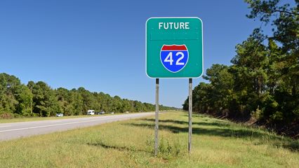 Sign advising motorists that this road is planned to become an Interstate in the future.  Surprisingly, "Interstate" is plated over on the sign, and the red portion on the Interstate shield does not contain the word "Interstate".