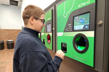 Elyse places a bottle inside the machine for recycling and gets a voucher for five cents.
